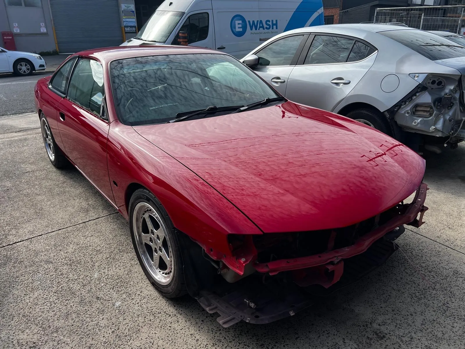 Red coupe freshly painted outside the workshop, before the front bumper is refitted