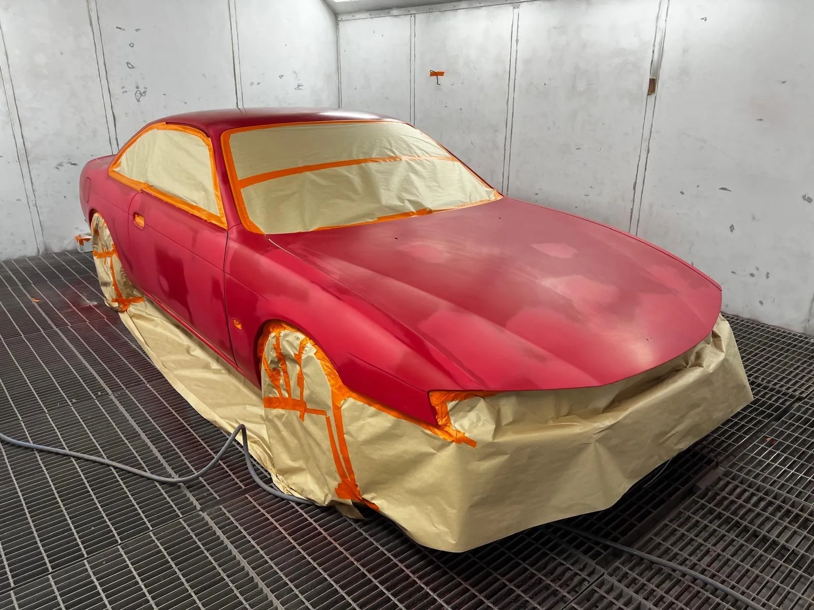 Red coupe masked for a respray inside the spray booth
